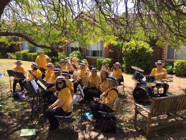 Maffra Municipal Band members in uniform, in position, with instruments in hand and ready to play in an outdoor setting under a tree