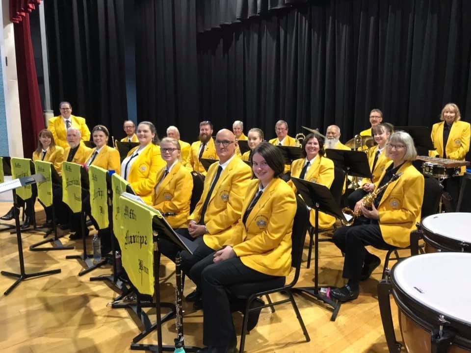 Maffra Municipal Band members in uniform, in position, with instruments in hand and ready to play on a hall stage